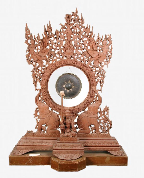 A carved wood stand with a gong in the center. It features an elephant on each side of the central figure holding the mallet.