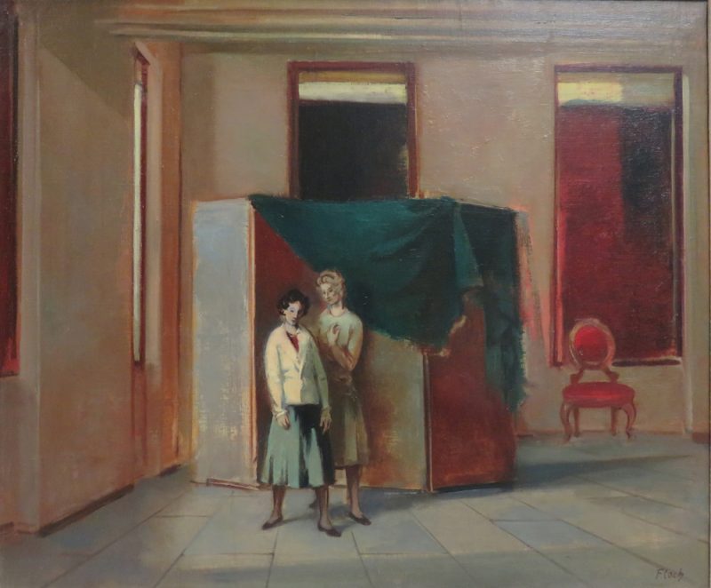 Two women stand in front of a brown screen and a chair in a room with two tall, narrow and dark windows.