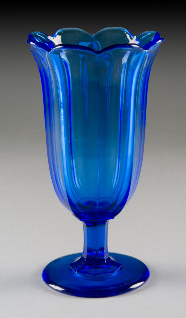 Trumpet-shaped vase with 8 vertical panels around sides. Rim scalloped & flared. Octagonal paneled stem. Flat, circular foot. Smooth pontil mark. Transparent blue. No disk. Molded in one piece.