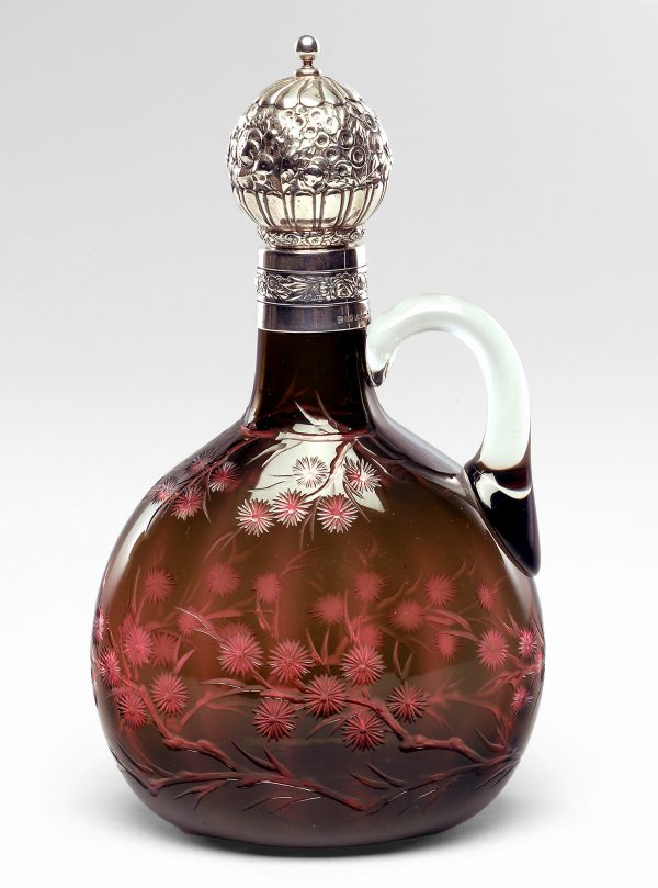 Pinched globe-shaped jug with cut plum blossom pattern on shoulder and lower body.  Thick C-shaped handle extends from neck to shoulder.  Silver mount on neck with decorative floral band.  Cork stopper with decorative floral patterned silver ball.  Color:  transparent green cased over rose; colorless handle.