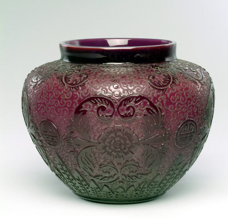 Urn-shaped vase with short, plain, cylindrical neck. Body with acid-etched 'Chang' design (Dimitroff, #6112, pg. 276). Plain, flat base. Color: Plum.