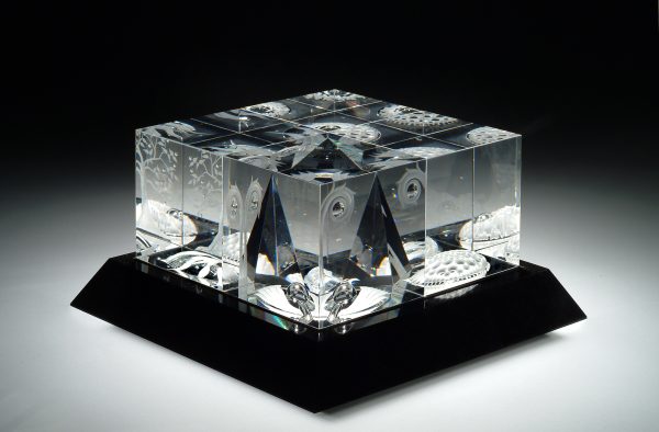 Four cubed sculpture inspired by Eric Hilton's 1975 Innerland. It is engraved with symbolic imagery suggesting the unity of creation, time, space, and the cosmic order. The cubes reflect a constantly changing panorama of images invoking earth, sea, sky, and the universe within and beyond.