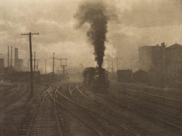 A train engine is seen from the front with black steam coming from the engine. Train tracks fill the foreground and telephone poles and buildings are in the background. Number 1, January 1903 Photographs: six by Gertrude Käsebier; one by Alfred Stieglitz, Hand of Man; one by A. Radclyffe Dugmore. Paintings: one by D. W. Tryon; one by Pierre Puvis de Chavannes.Texts: by Alfred Stieglitz, Charles Caffin, Dallett Fuguet, John Barrett Kerfoot, Sidney Allan (Sadakichi Hartmann), Edward Steichen, Joseph Keiley, and others.