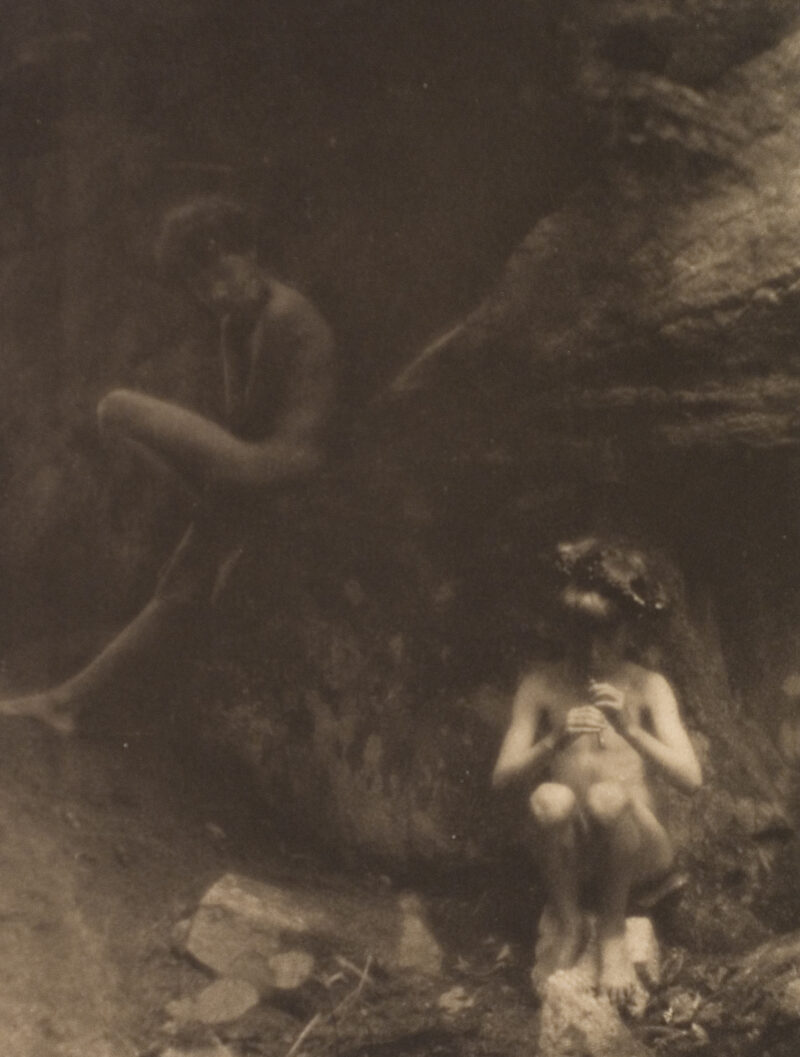 Two children sit in a rocky landscape. The one in the foreground plays a pan pipe and the other looks on with his chin in his hand.