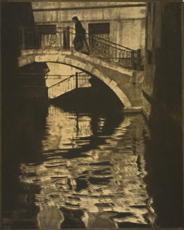 View of a bridge over a canal in Venice with a woman at the top center of the bridge. Number 21, January 1908Photographs: twelve by Alvin Langdon Coburn. Texts: (unsigned) 