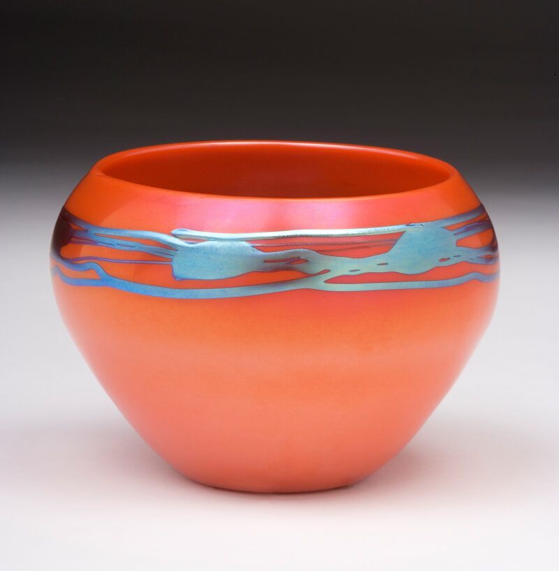 A squat vase shape of rouge flambé glass with a blue free-form design on the shoulder.