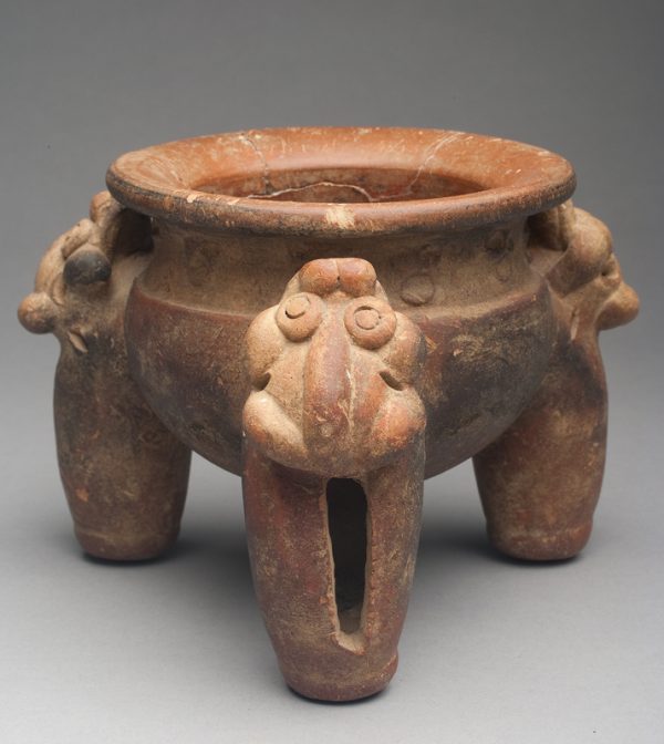 Buff body with terra cotta wash. Legs are topped with frogs, other decoration along shoulder of bowl. Legs include a rattle.