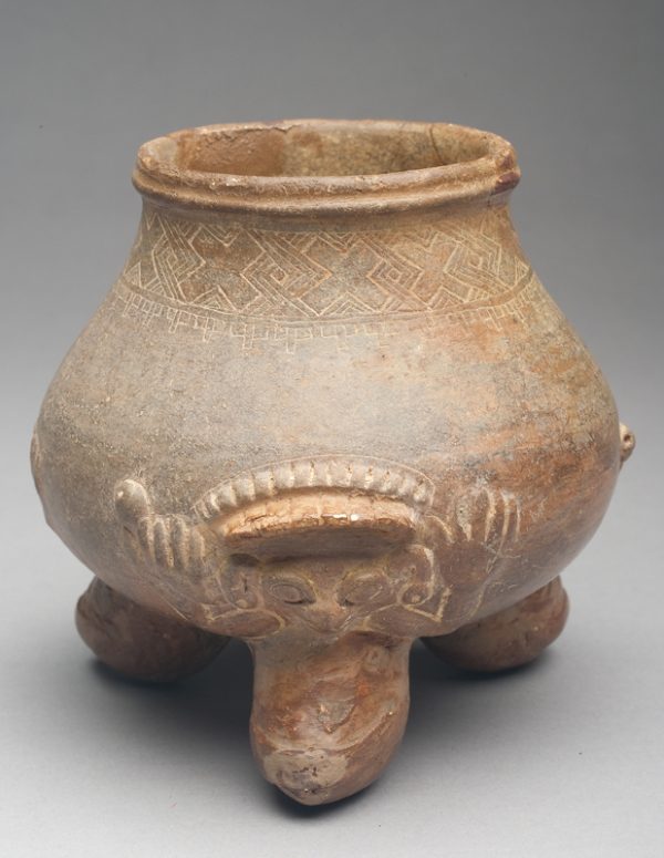 Buff body with medium gray surface and reddish feet. The legs have an animal sculpted above them. The animals all have earrings, headdress and rattle in their right hand. There is a geometric design incised in the neck of the bowl.