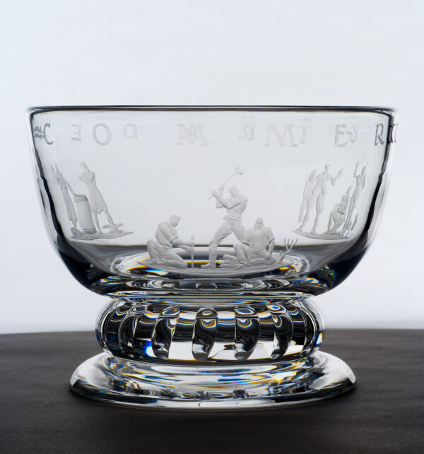 Clear bowl with large foot that has etched on its sides images of workers involved in 