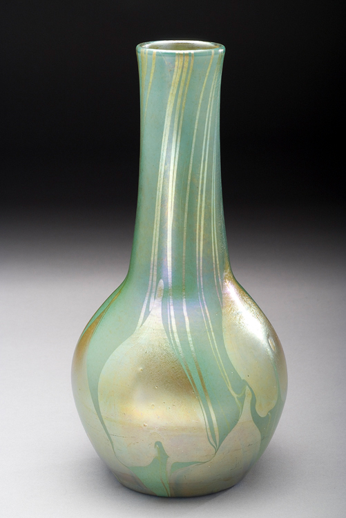Vase has elongated neck with bulbous bottom. It has a milky green background glass decorated with gold iridescent leaves and vines with tinges of lavender.