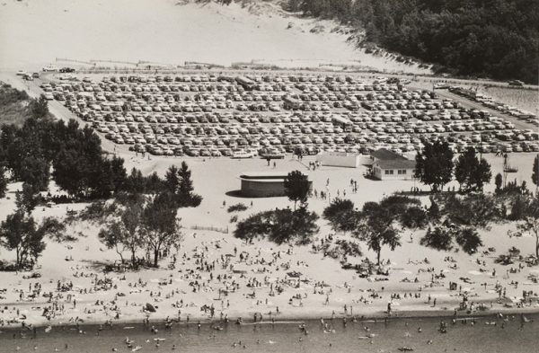 Beach with swimmers in the foreground and parking lot in background.