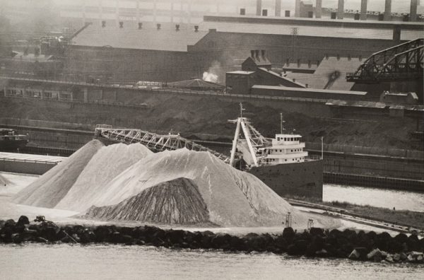 A steel mill with ship on river offloading materials into giant piles.