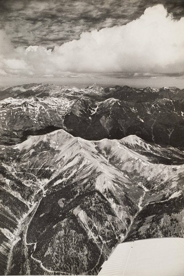A mountain range with snow in valleys and peaks. Clouds are in the sky.