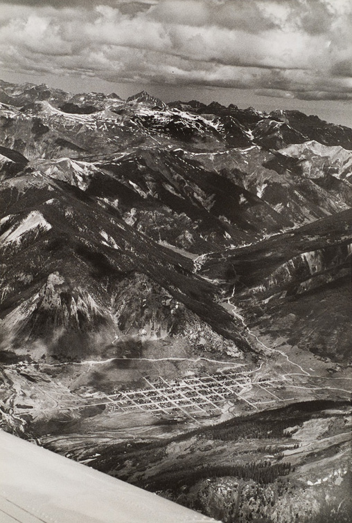 Mountains with snow in the background, small city in a valley in the foreground. The plane’s wing is visible at lower left.