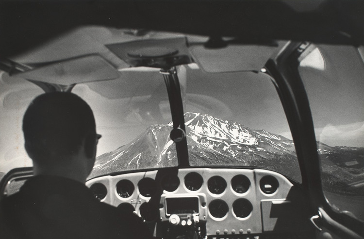 View of cockpit with pilot and Mount Shasta through windshield.
