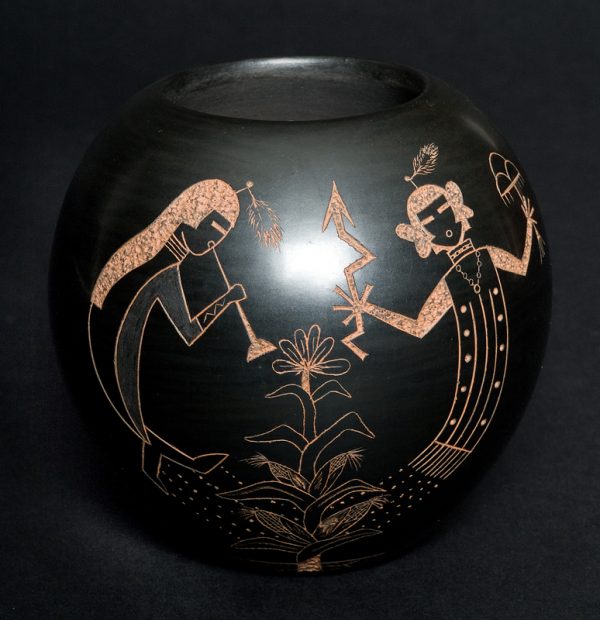 Flat bottomed bowl polished black with sgraffito showing red clay. The images are Kokapelli and Corn maiden with cornstalk between.