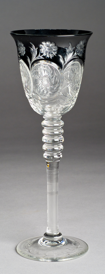 A clear goblet with the bowl pressed with foliage design and black background of flowers at rim.