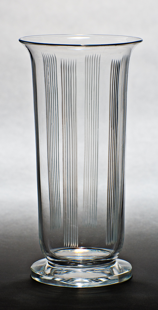 A tubular shaped vase with squat foot and flared rim. There are six sets of seven vertical lines.
