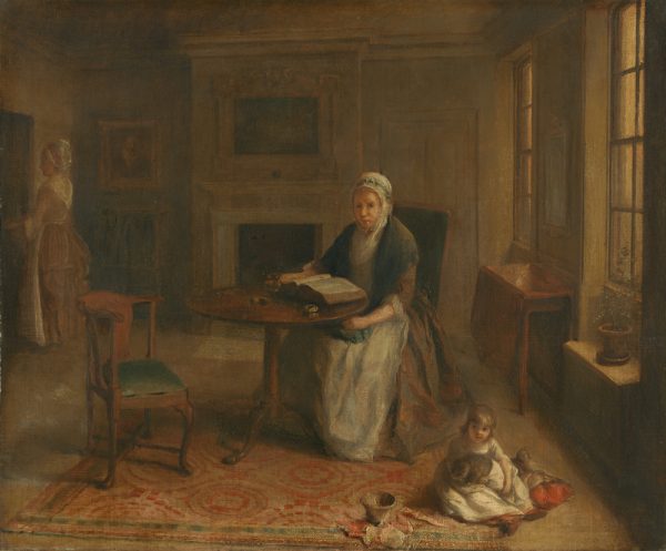 A woman sits a a table in the center of the room. She is reading from a large book. A small child sits on the floor, at lower right, playing with a kitty.