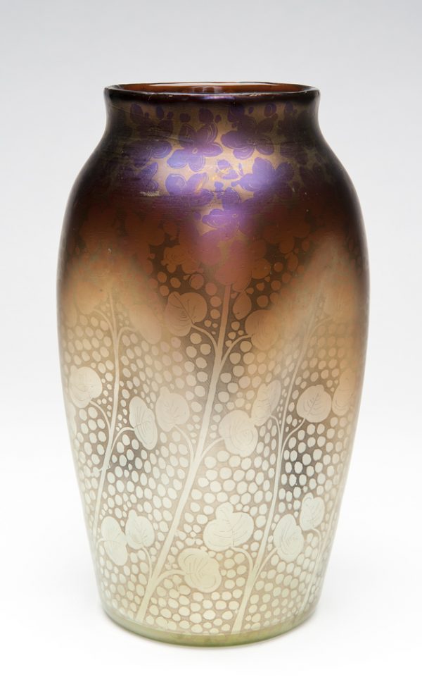 A square vase with sides curved in and rounded edges with a circular rim. The decoration is diagonal stems with leaves on a dot background. The color is a gradation from light at the bottom to dark at the top; gray/green on clear to mauve on opaque gold iridescent.
