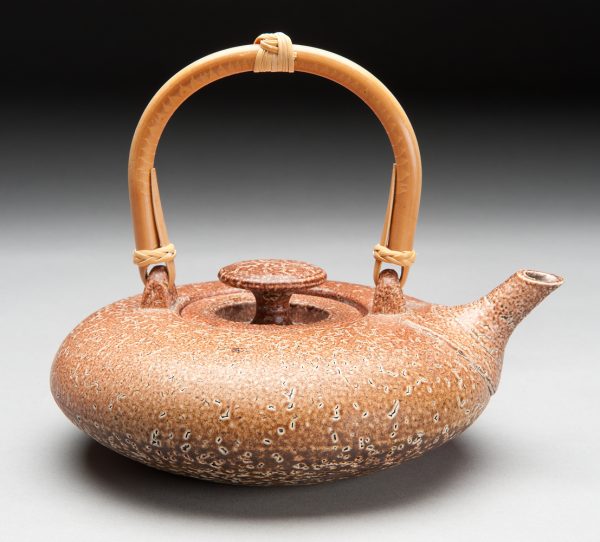 A functional thrown teapot with a salt-glazed, rust and dark brown surface. The teapot shape is squat with a bamboo handle.