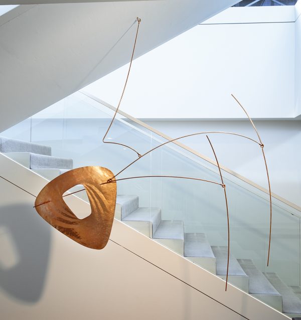 An abstract hanging mobile of a flat oblong disk on the two curved rods on the right.