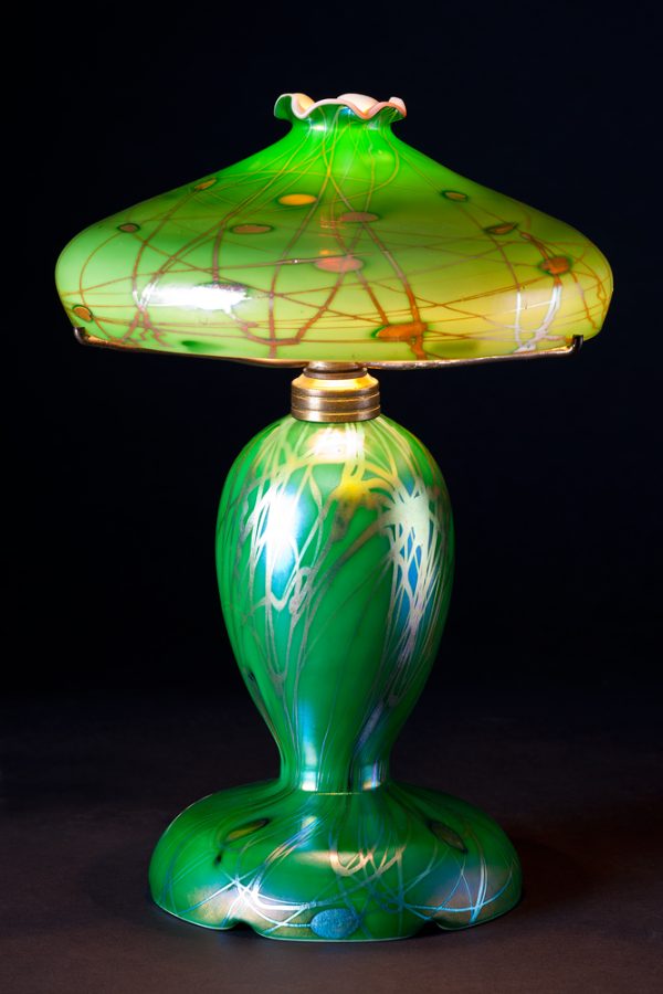 A lamp comprised of decorated green Aurene over calcite, the shallow shade with tapered, ruffled opening, the decoration depicting silvery iridescent leaves and vines.
