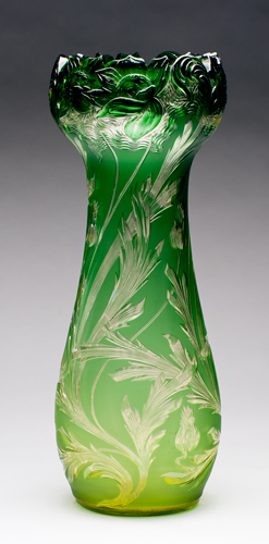 A green over clear cut crystal vase. The form is rounded at bottom and flared at top with a rim shaped to match the floral decoration.