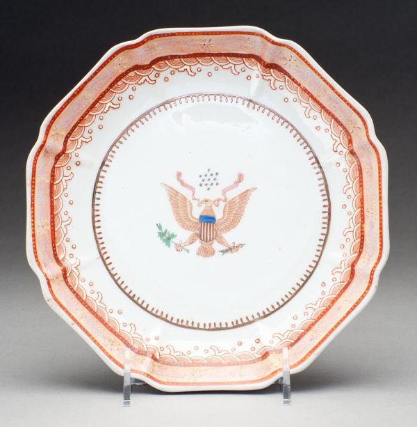 At the center of the plate is a symbolic eagle with red gold and blue flag on body,one claw holds arrows and the other green foliage, there are stars above the head and a ribbon behind. The border has a wave pattern.