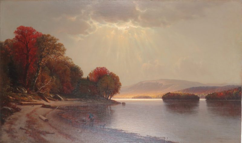 A landscape of a lake over which the sun breaks through clouds shinning on tall red and gold trees at the left and a low mountain on the right. There is a man with a rowboat and small dog in the foreground on the curved shoreline.