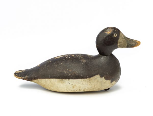 A painted wood decoy with black head and back, white belly, and gray bill.