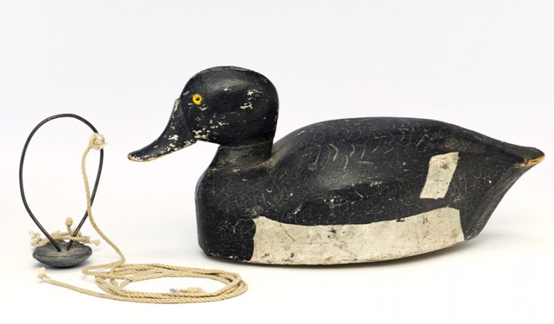 Painted wood, black with white ringed neck and at belly and wingtips. A round metal weight is separate from the decoy.