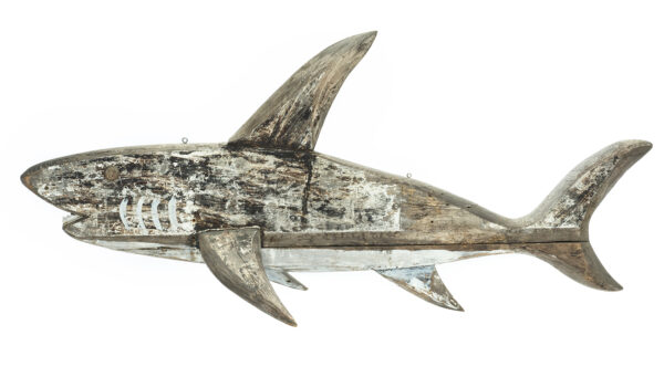 A decorative hanging in the shape of a three dimensional shark. The shark is made of cut, shaped, and assembled pieces of wood. They are held together with iron-alloy nails. The sharks teeth are cut out of non-ferrous white metal (est. aluminum alloy) sheet. The shark is painted overall on both sides and would have been suspended via two eyes crews at the top of the construction.