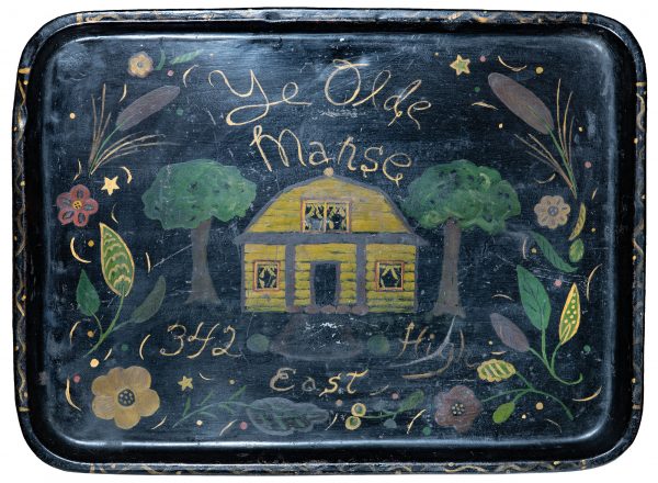 Tole painted on a tin tray of a yellow house between two trees.