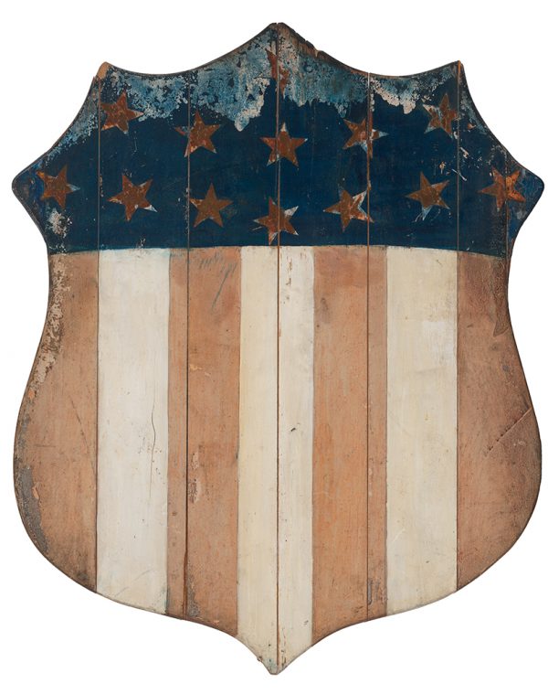 Painted wood shield-shape in red and white stripes at bottom. There were 13 stars made of gold foil paper over blue on top. Shield made of narrow slats of wood held together by two batons rivets and leather.