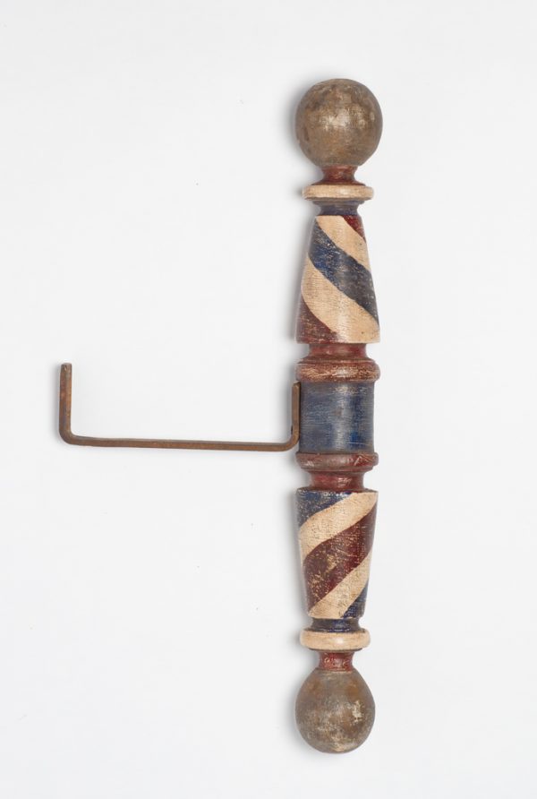 A barber pole with attached mounting bracket. The pole is made of one piece of turned wood that is smoothly finished and painted with red, white, and blue paint. The top and bottom balls have no paint.