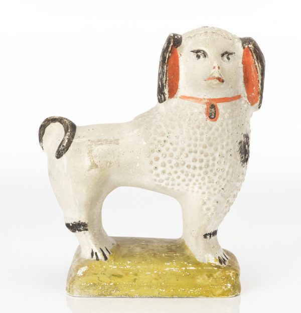 A mold made chalkware figure of a dog with painted features: black eyes, ears and tail. Red inside ears and on collar.