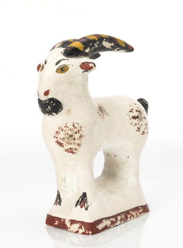 A mold made chalkware figure of a white goat with black and tan horns, black eyes, tail, and hoofs.