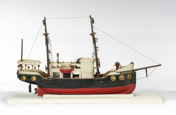 A model ship made primarily of carved and painted wood. Metal chains, anchors, and other detailed elements are present. Carved wooden mast and spars support a connected network of rigging and chains. The rigging components are wire wrapped with paper or fiber.