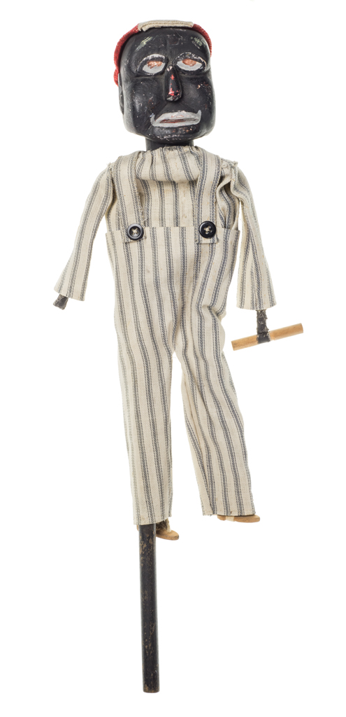 A stick puppet of a man wearing overalls and shirt made of pillow ticking with a red and white beanie.