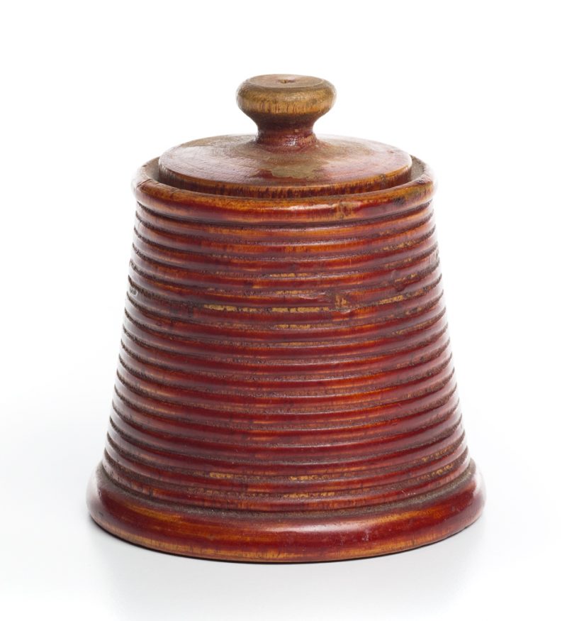 A red treen ware in beehive shape with lid. The sides have turned repeating rows.