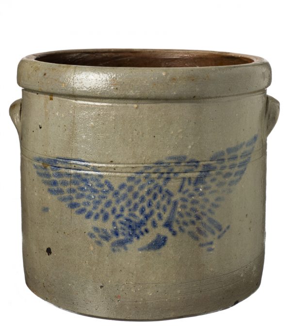 Tan crock with blue stencil of flying eagle. The crock has two lug handles and dark interior.