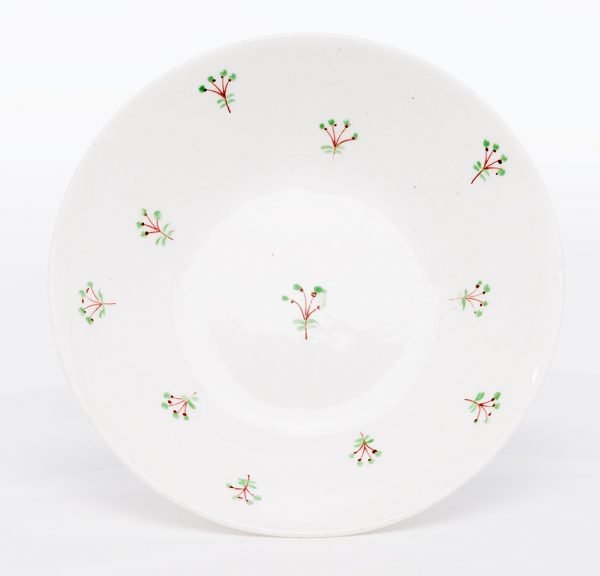 A small ceramic saucer with clear speckled high-gloss glaze and sprig pattern overglaze. The ceramic body is white and translucent, likely porcelain.