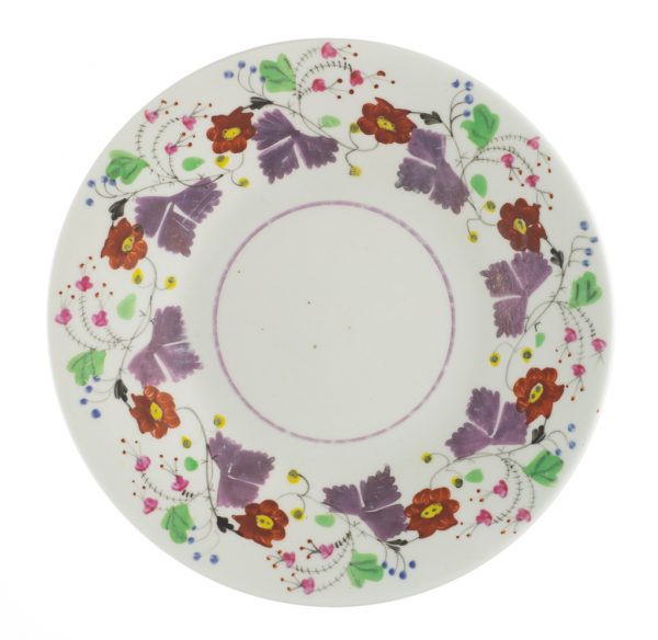 A small saucer with lustre glaze in stylized lilac-color leaves, red flowers, and green leaves circle the rim.