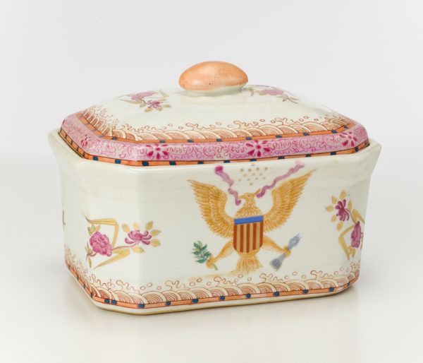 An octagonal lidded dish. The long sides depict an Eagle with arrows in one talon and olive branch in the other, a red ribbon in
his beak and a red, gold, and blue shield in front of his chest. The diagonal sides have rose sprays in red and gold. The border on the lid is highly ornamental in pink, orange, and blue.