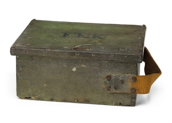 Lidded wooden box with a leather hinge and strap. Interior storage compartments are lined with fabric. The exterior is painted green overall with the letters FEK in black on the top.