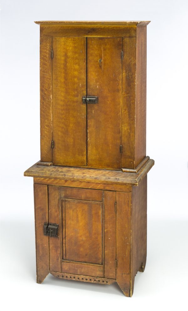 A small two tiered cupboard with two cabinets, one on each tier. There are decorative latches with geometric patterns: one on each cupboard. The exterior of the cupboard has a faux painted surface finish with yellow comb painting below a natural resin varnish.