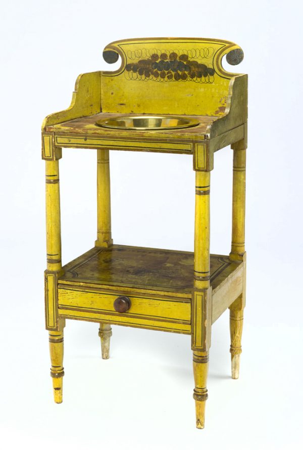 A freestanding wash stand made of turned, carved, and joined wood that is painted yellow overall. A separate bowl is inserted into the top.