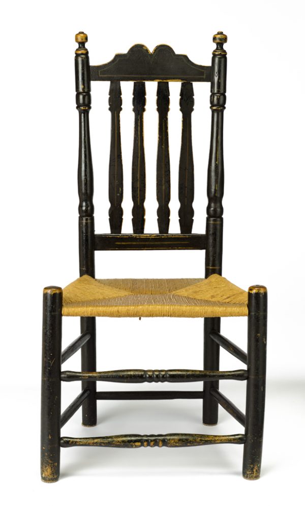 A banister side chair with turned stiles and legs, seven turned stretchers, and a woven rush trapezoidal seat. 
The wooden structure is painted overall with black paint.