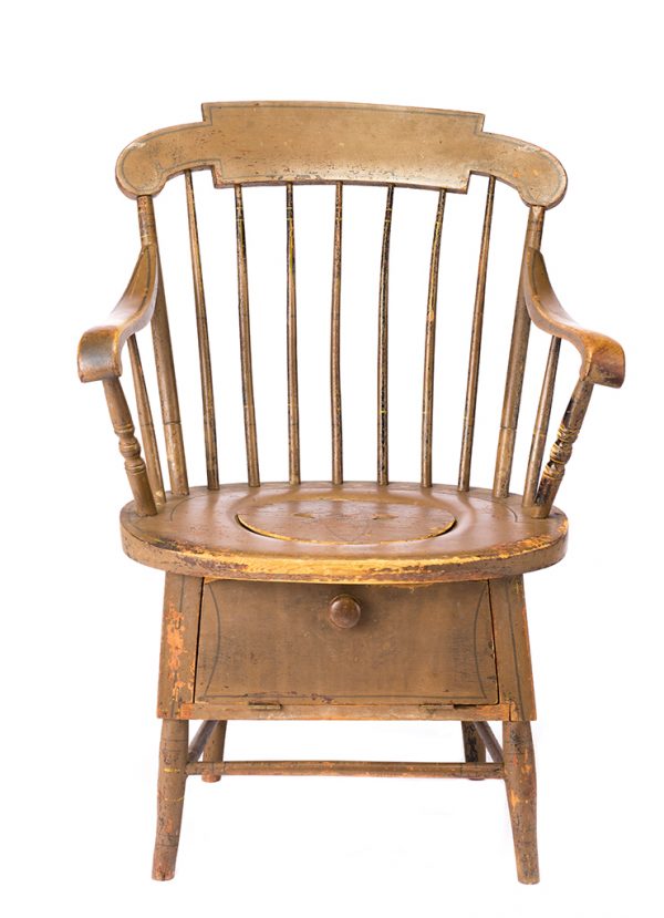 A large chair with 7-spindle back and legs. The seat of the chair has a large hole with lid to be used as a commode. A small closed cabinet is below which would have originaly held a bowl. The paint colors are yellow ochre over salmon underpaint, and layer of black underpaint. There is line decoration in black, gray/green and yellow.